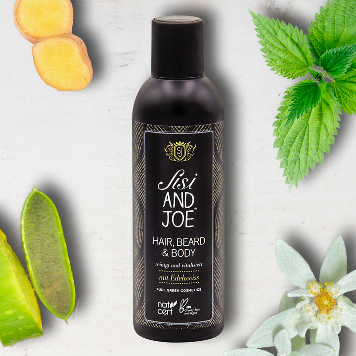 „Sisi and Joe“ Hair & Bodywash Flasche umgeben von Ingwer, Brennnessel, Aloe Vera, Edelweiß; Bio, vegan, mit Apfel- und Brennnessel-Extrakt für sanfte Reinigung und Frische.