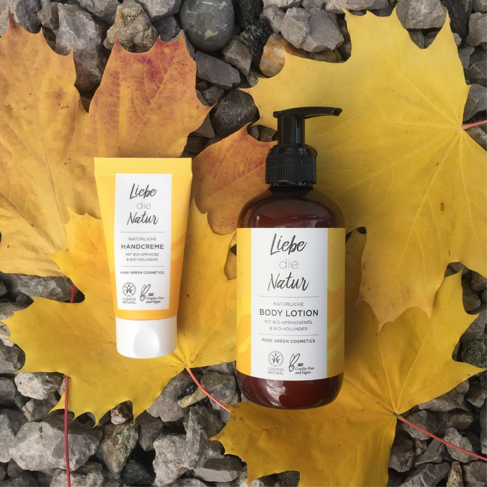 Liebe die Natur Bodylotion mit Aprikosen- und Holunderextrakt, Bio & Vegan, neben passender Handcreme, auf gelben Ahornblättern präsentiert.