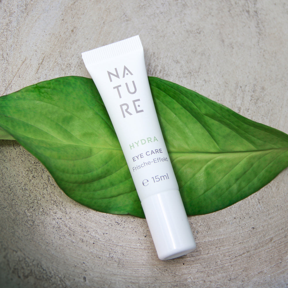 NATURE Hydra Augencreme mit Gurkenwasser & Hyaluronsäure, 15 ml, in weißer Tube auf grünem Blatt, bietet intensive Erfrischung und Pflege für die Augenpartie.