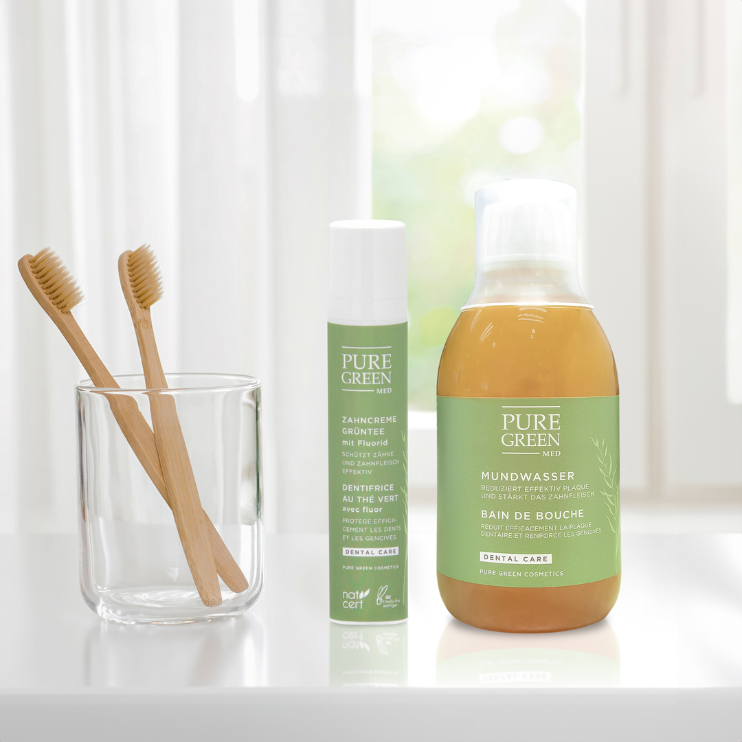 Ein Badezimmer-Countertop mit zwei Bambuszahnbürsten im Glas, einer Tube grüner Tee Zahncreme und einer Flasche Mundwasser, beide von PURE GREEN MED.