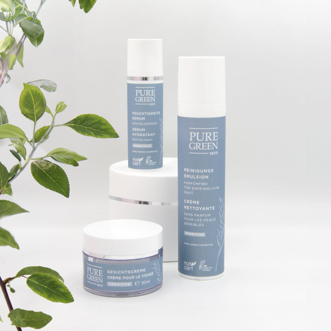 Drei PURE GREEN MED Produkte: Gesichtscreme, Feuchtigkeits-Serum und Reinigungs-Emulsion auf weißer Fläche, dekoriert mit grünen Blättern. Dezentes, reines Design.