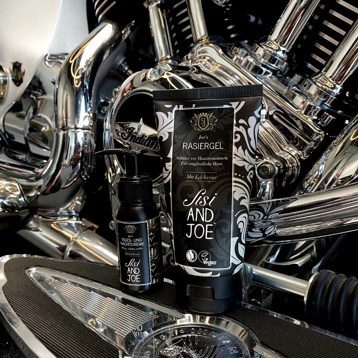 Nahaufnahme eines Motorradmotors mit zwei Behältern auf der Fußraste: Sisi and Joe veganes Rasiergel mit Kamille und Edelweißextrakt und Tages- und Nachtcreme, beide vegan.