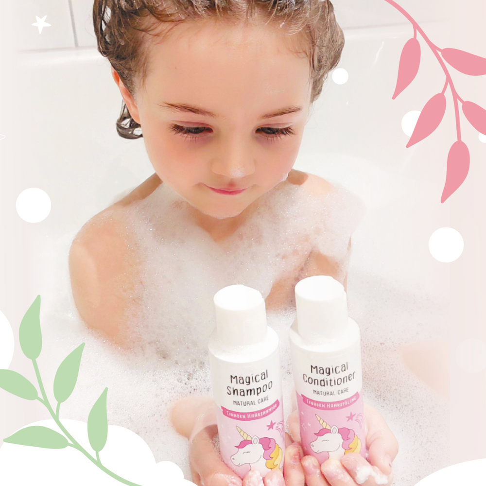 Ein Kind im Schaumbad hält Magical Shampoo und Magical Conditioner mit Einhorn-Illustration. Haarbalsam mit Heidelbeerextrakt für leichte Kämmbarkeit und seidig-weiches Haar, vegan.