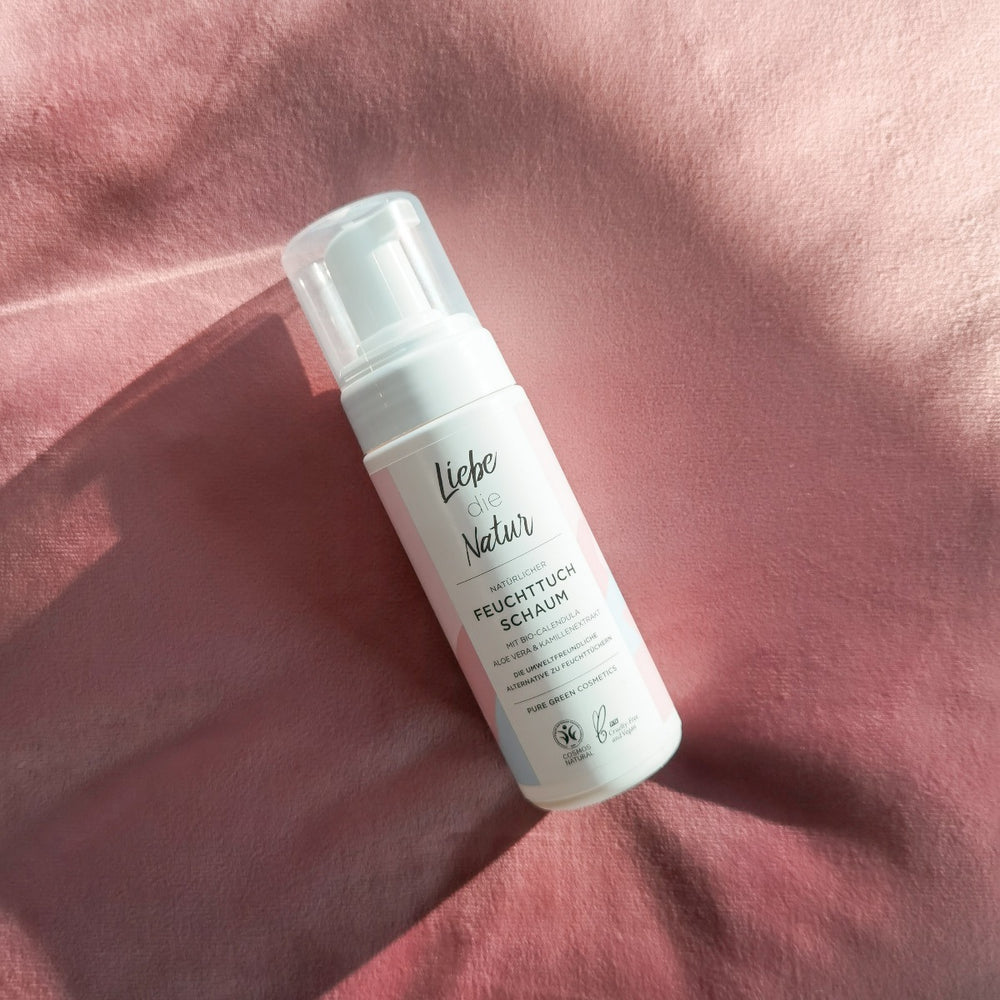 Liebe die Natur Feuchttuchschaum mit Aloe-Vera und Calendula, pflanzliches Reinigungs- und Pflegeprodukt, vegan und biologisch, auf rosa Stoffhintergrund.
