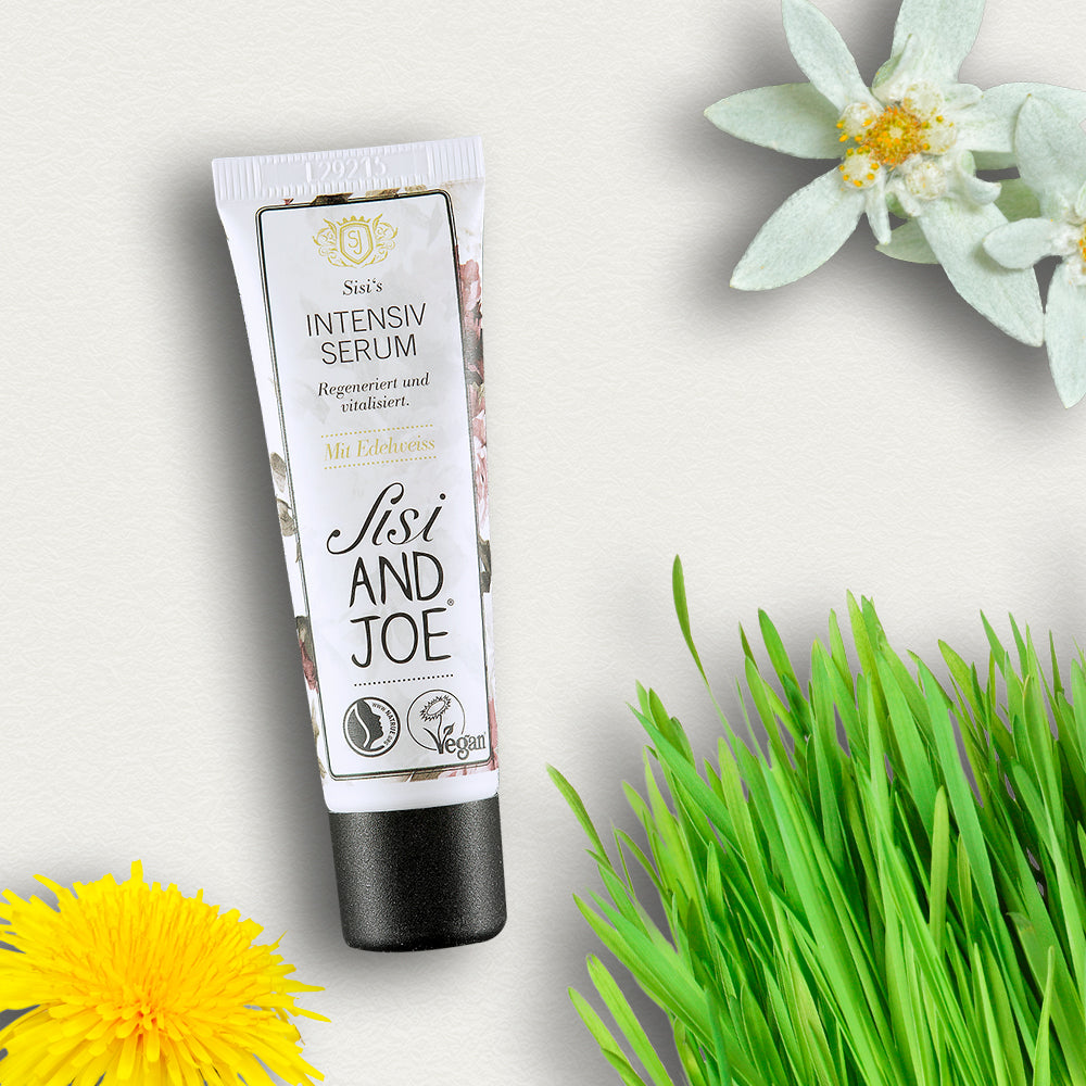 Tube des Edelweiß-Intensiv-Serums mit Hyaluronsäure & Q10 von Sisi and Joe, umgeben von Edelweiß, Löwenzahn und Gras, für intensive Regeneration und strahlenden Teint.