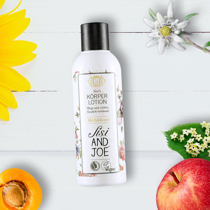 Edelweiß-Bodylotion von Sisi und Joe auf Holz, umgeben von Sonnenblumenblüten, Edelweiß, Holunderblüten, Apfel und Aprikose; vegan und tierversuchsfrei.