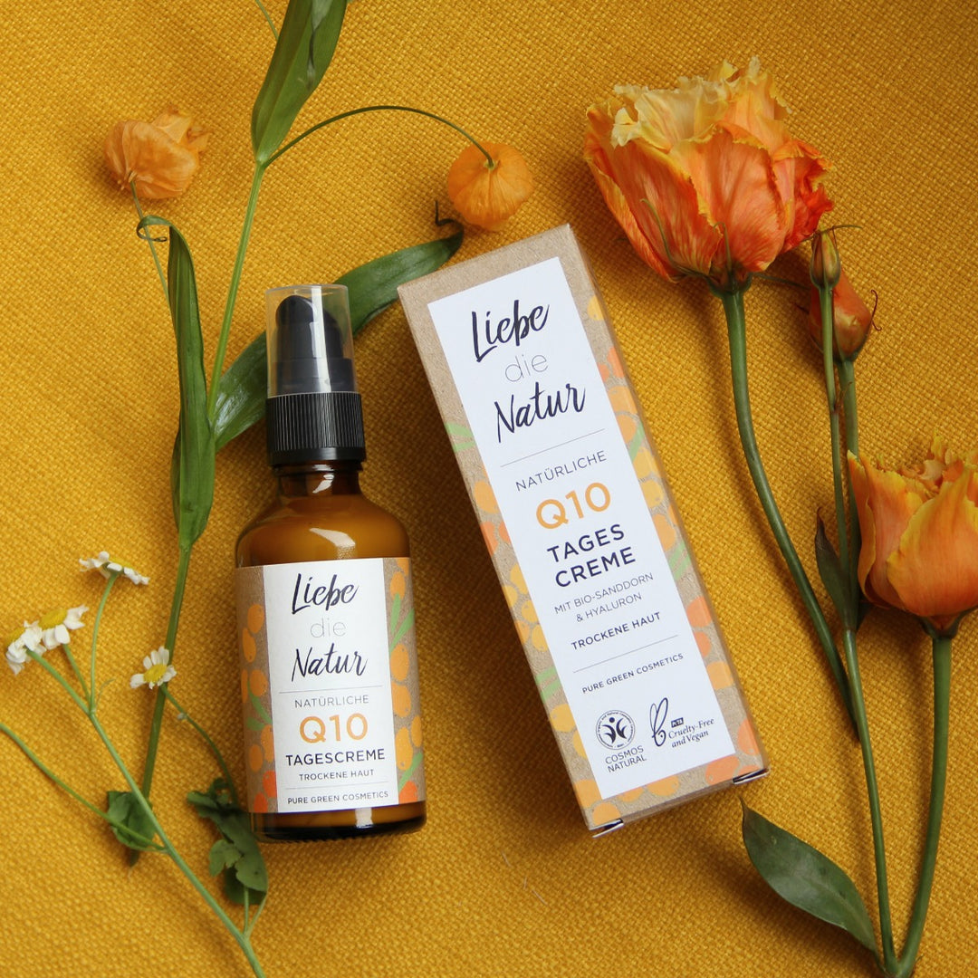 Q10-Tagescreme mit Bio-Sanddorn & Hyaluronsäure, pure green cosmetics, Glasflasche mit Pumpverschluss und Karton, vegan und tierversuchsfrei, begleitet von Blumenakzenten.