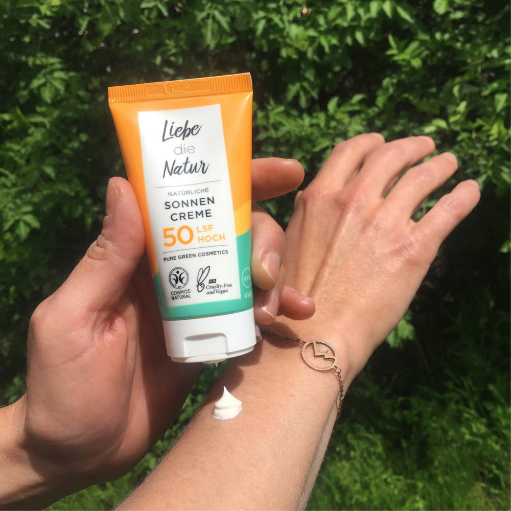Person hält Sonnencreme LSF 50 mit Zinkoxid & Sonnenblumenöl von Liebe die Natur, trägt Creme auf den Arm auf. Verpackung: Vegan, cruelty-free.