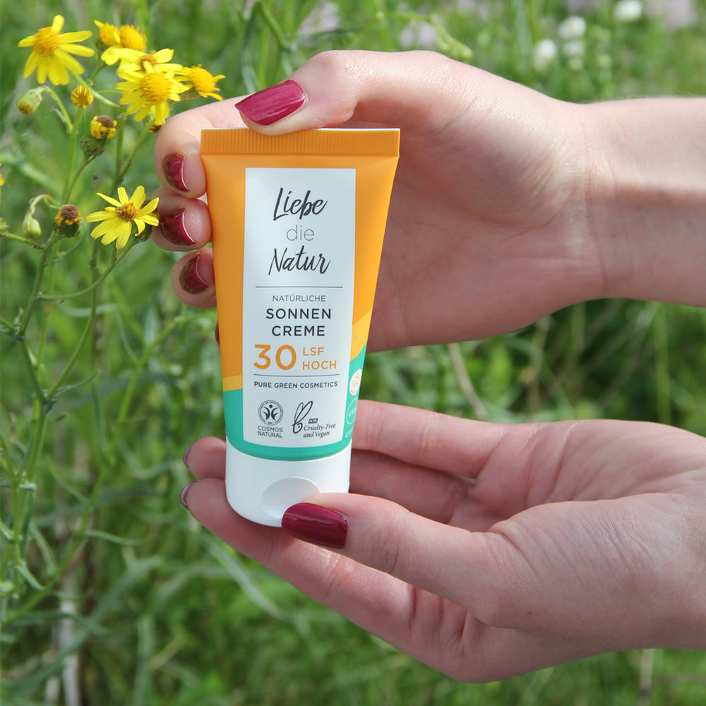 Hände halten eine Tube Sonnencreme LSF 30 mit Zinkoxid & Sonnenblumenöl für mineralischen UV-Schutz & intensive Feuchtigkeit | Bio & Vegan, umgeben von Wildblumen.