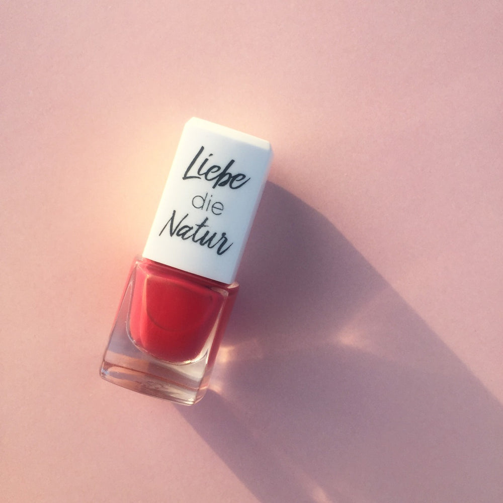 Glasflasche mit rotem Nagellack, weißem Deckel Liebe die Natur, auf rosa Fläche. Wasserbasierte Formel mit natürlichen Farbpigmenten, bio und vegan.