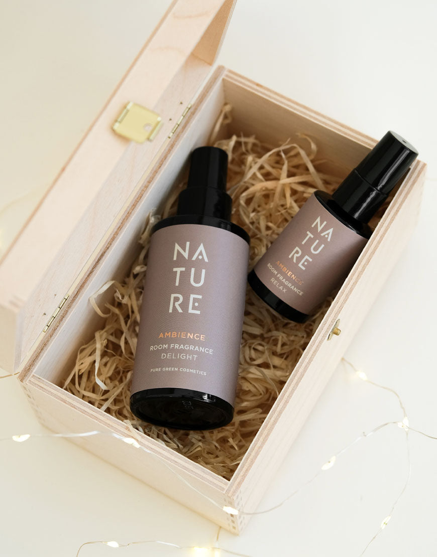 Geschenkset für Wohlfühlmomente mit exklusiven NATURE Raumdüften in einer Holzkiste, enthält zwei Amber-Glasflaschen: Raumduft Delight und Relax, umgeben von Lichterkette.