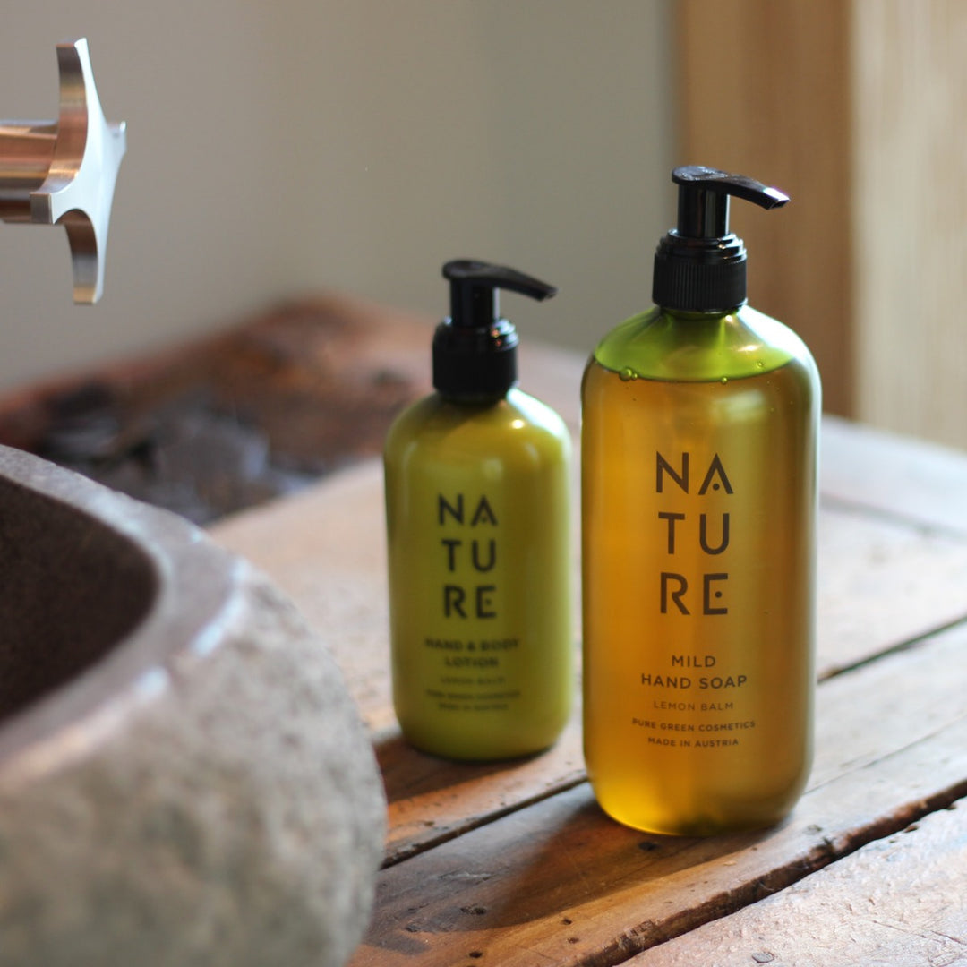 Zwei Spenderflaschen auf einem rustikalen Holzuntergrund zeigen Handseife mit Sonnenblumenöl & Lindenblütenextrakt und Lotion, beide bio und vegan, neben einem Steinsink.