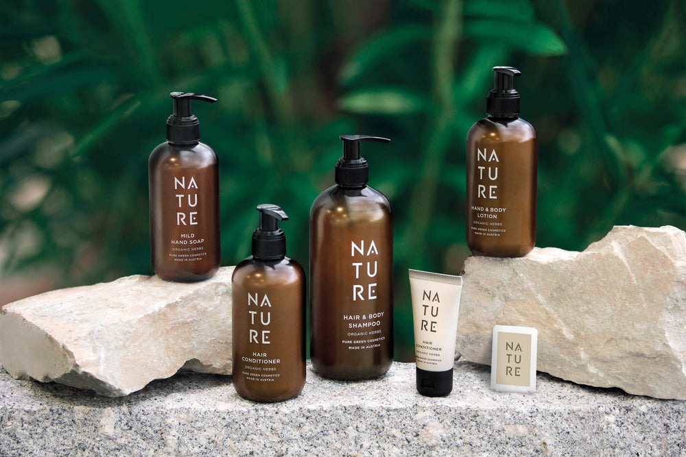 Sammlung von NATURE-Pflegeprodukten, darunter Bodylotion mit Alpenkräutern für eine gepflegte und gesunde Haut | Bio & Vegan, neben anderen Seifen- und Shampoo-Flaschen.