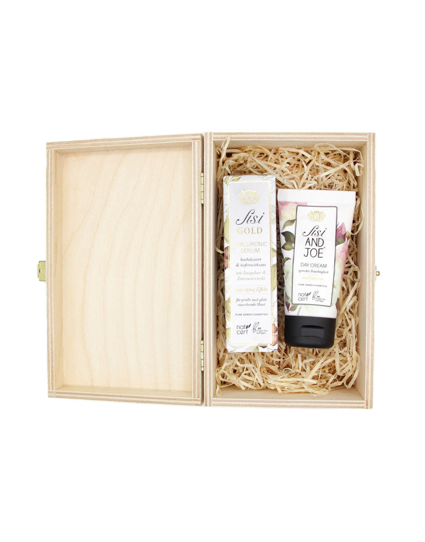 Beauty‑Geschenkbox mit Hyaluronserum & Tagescreme, präsentiert in einer offenen Holzbox mit Naturfasern, enthält Sisi Gold Hyaluronic Serum und Sisi and Joe Day Cream, bio und vegan.