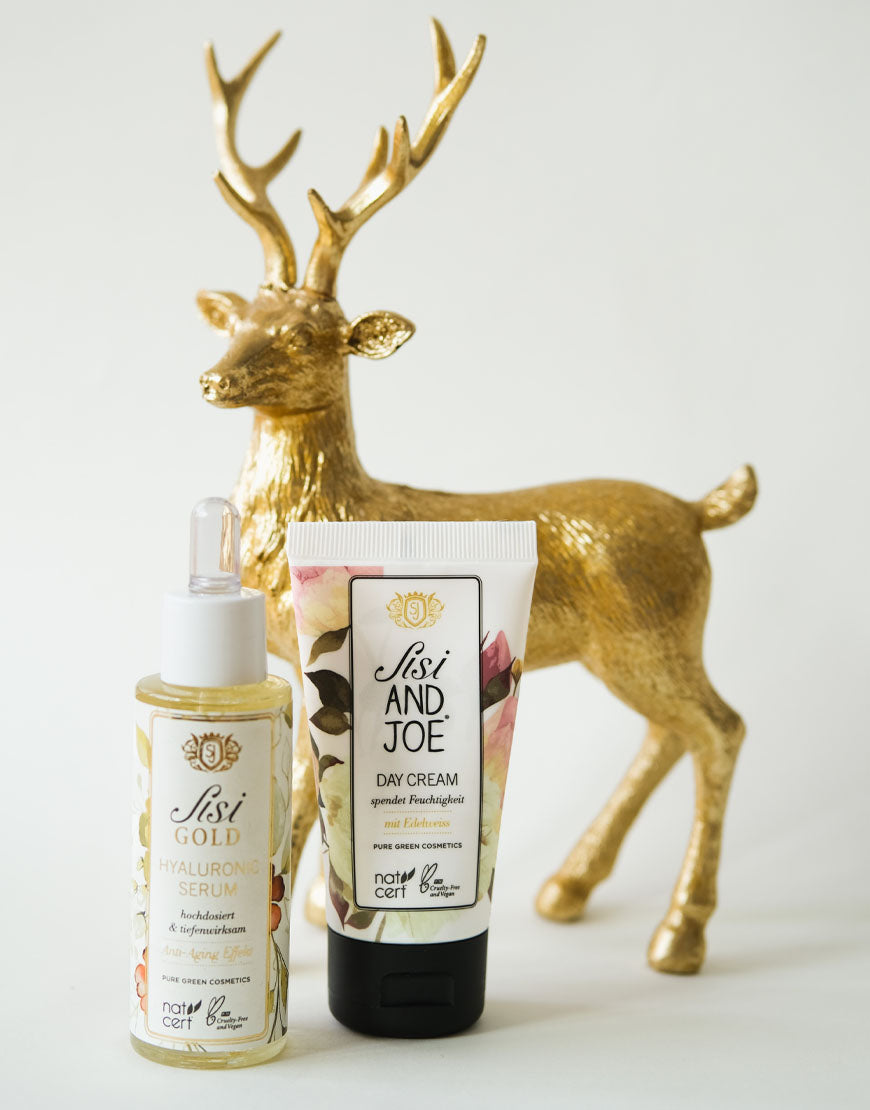 Beauty‑Geschenkbox mit Hyaluronserum und Tagescreme für intensive Feuchtigkeit und strahlende Haut; vegan und bio, mit goldener Hirschfigur im Hintergrund.