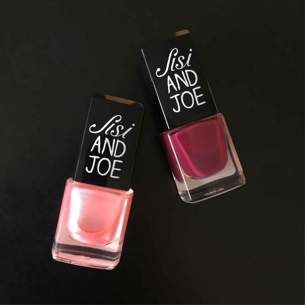 Zwei Glasflaschen Nagellack von Sisi AND JOE, eine in schimmerndem Rosa, die andere in tiefem Beerenrot, mit veganer, umweltbewusster Formel und schwarzem Deckel.
