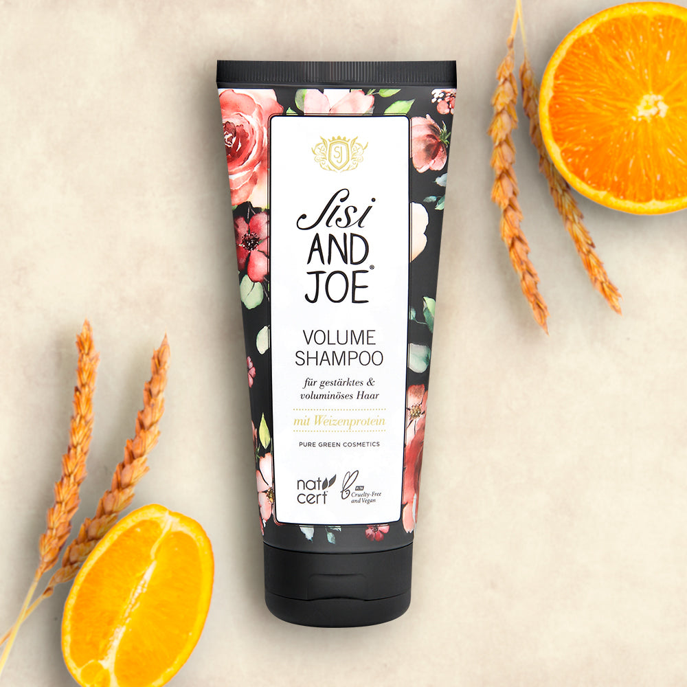 Protein-Boost Volumen Shampoo mit Weizenprotein und Süßorangenduft, vegan und cruelty-free, in einer grünen Tube neben Weizenstielen und einer halbierten Orange. Made in Austria.